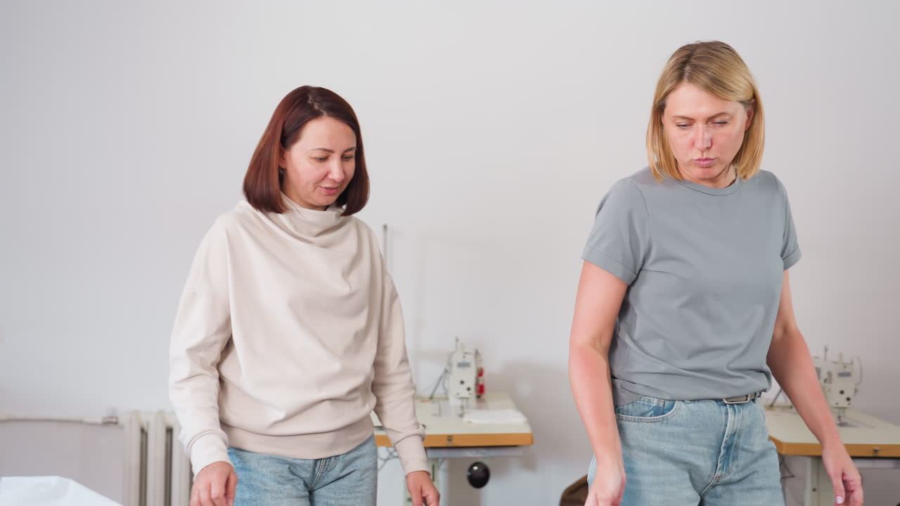 Two stylists moving toward workspace discussing ideas while picking colorful cloth pieces, preparing for fashion project in creative sewing environment with casual setup visible in background