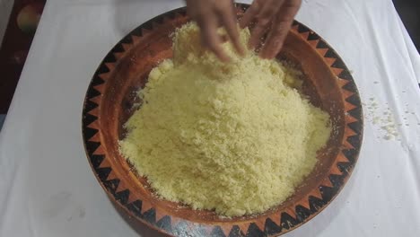 woman rolling hot semolina of couscous between her fingers in a wooden dish at home after steaming it