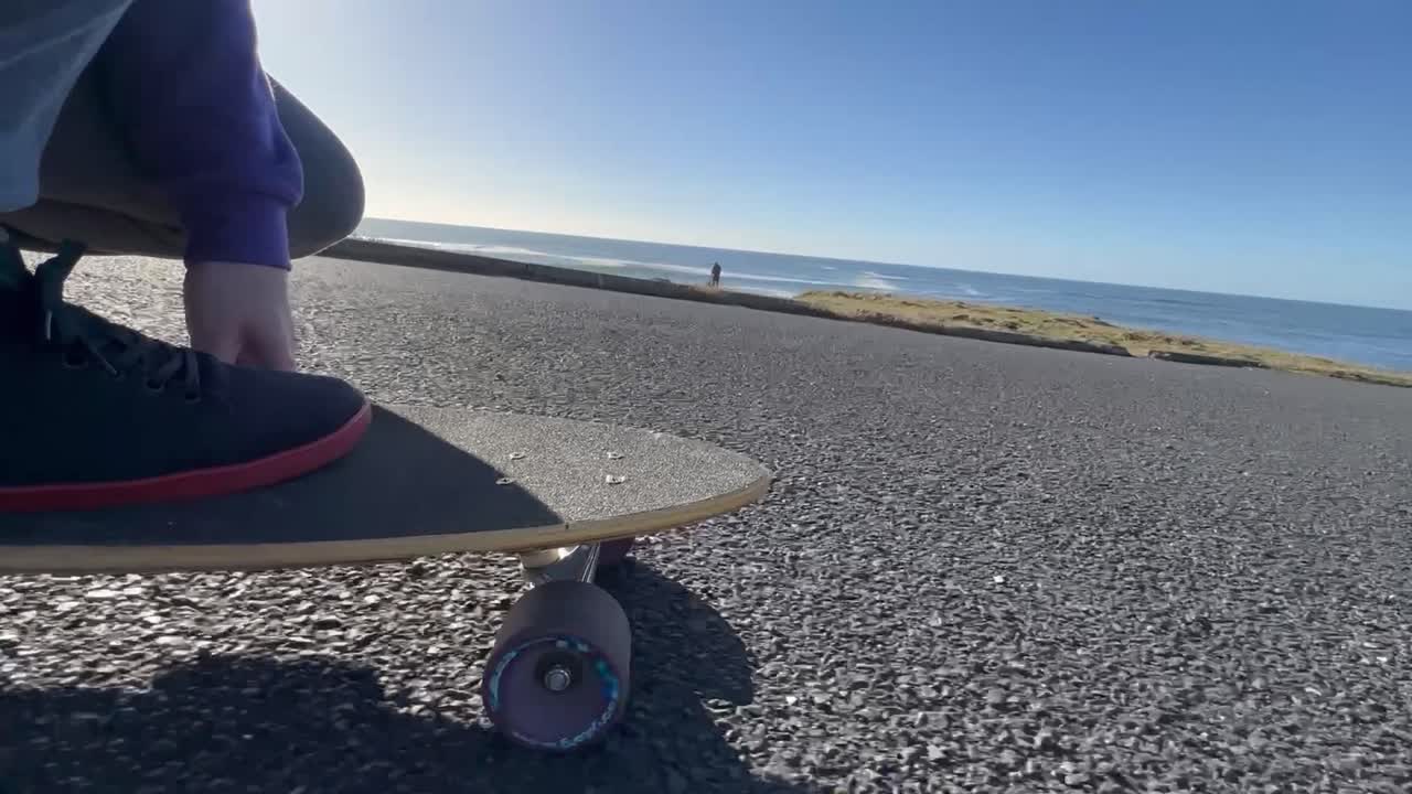 Slow motion ground level view of a skate board being ridden on a sunny day near the ocean.