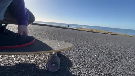 slow motion ground level view of a skate board being ridden on a sunny day near the ocean.