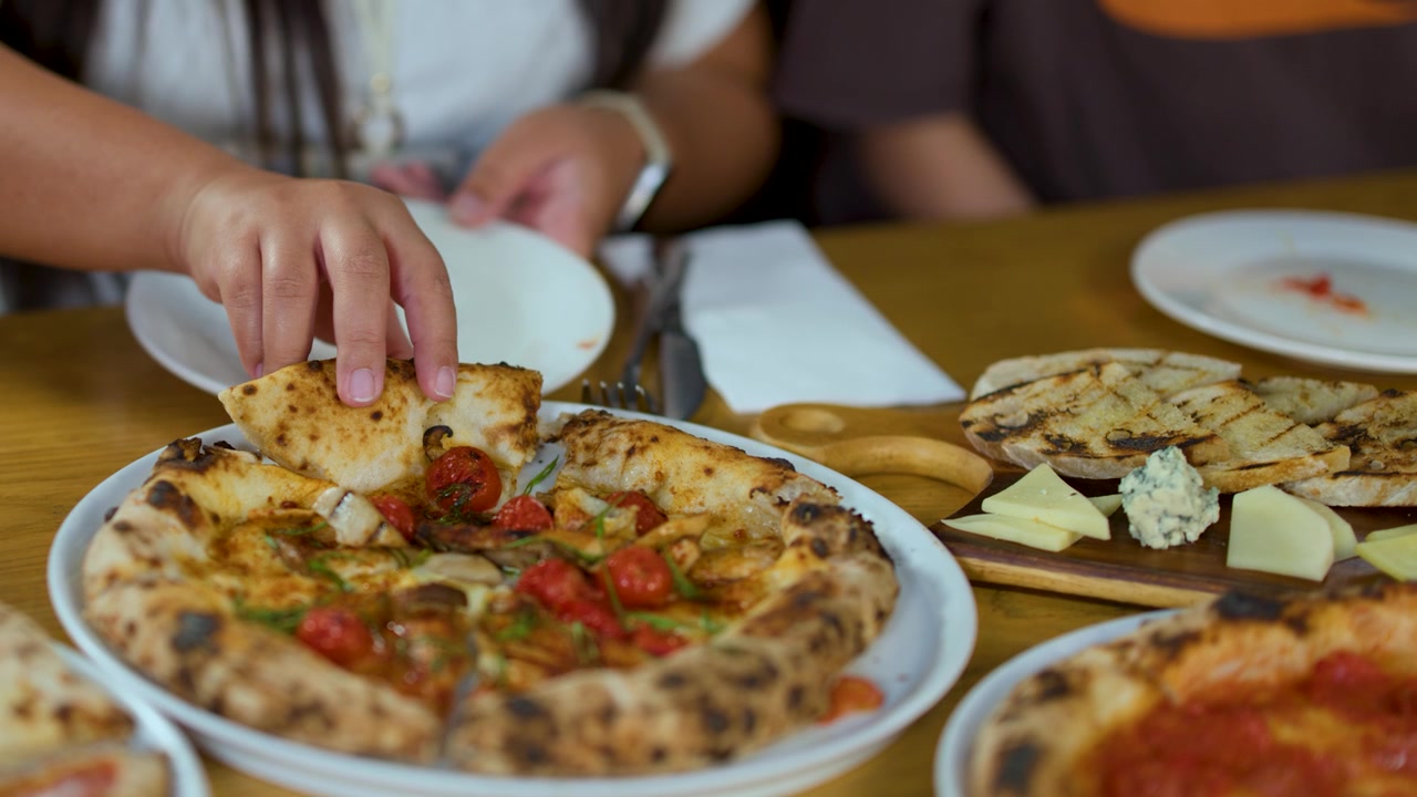 Primo piano di mani che prendono una fetta di pizza da un tavolo con antipasti italiani