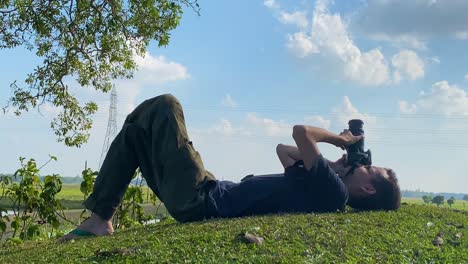 man lying on grass ground taking pictures of clouds in the sky, zoom out, day