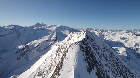 drone flying around top of mountain with snowy landscape in background on sunny day in austria