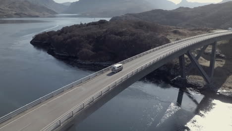 Aerial-footage-of-a-vintage-VW-campervan-driving-across-Kylesku-Bridge-on-a-sunny-day-in-Sutherland,-Assynt,-Scottish-Highlands,-Scotland