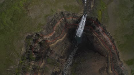 toma aérea de arriba hacia abajo de un barranco profundo y empinado con una cascada que cae en islandia durante el día - cascada hengifoss épica en el valle del cráter gigante