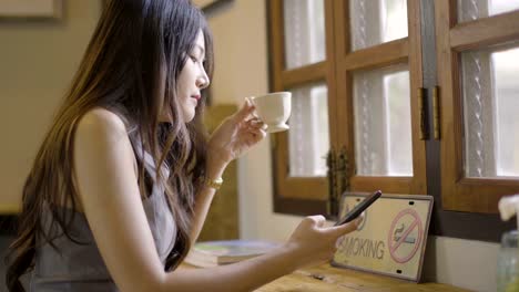 asian women drink hot tea and play phone in cafe.