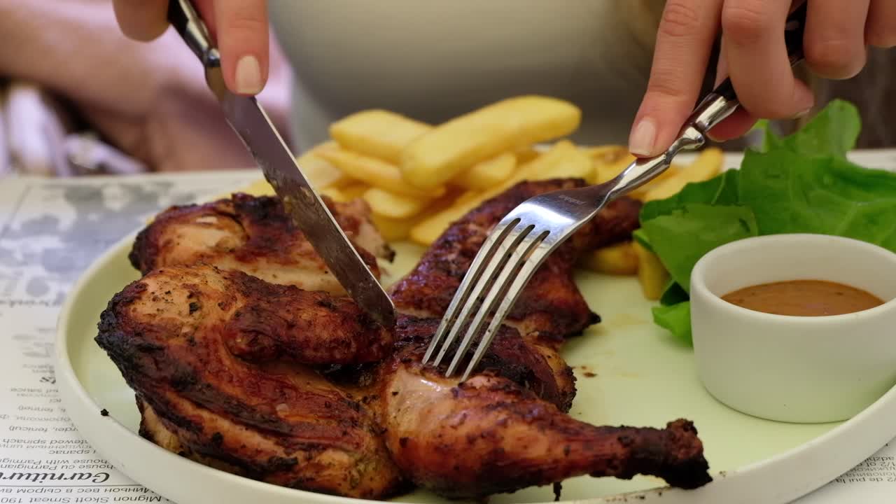 Woman cutting up a piece of grilled chicken with potatoes at a restaurant