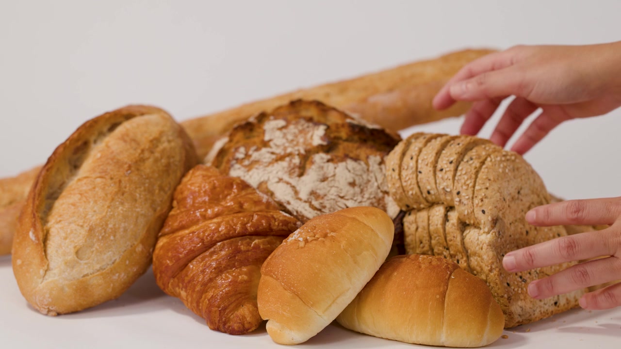 Close-up shot of hands organizing sourdough, baguettes, and croissants against a clean white backdrop.