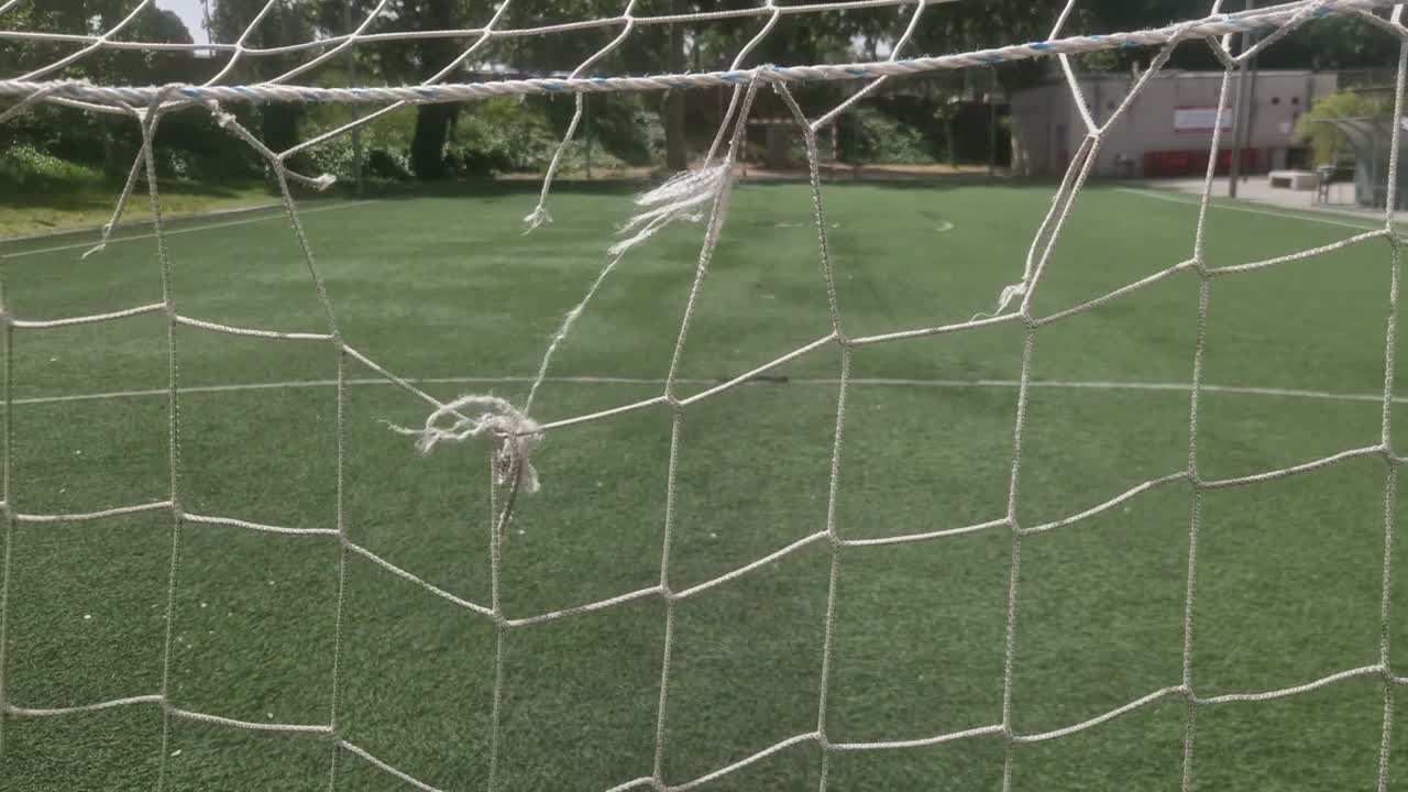 Boş, yeşil sentetik çim sahada yırtık ve kırık bir futbol kale ağının panoramik çekimi.