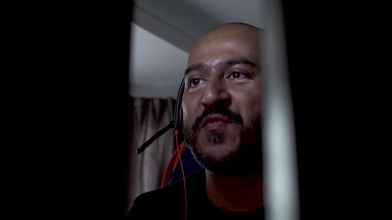 헤드셋을 착용한 대머리 인도 남성이 머리를 좌우로 흔들며 음악을 듣고 전화로 방해를 받고 있습니다.