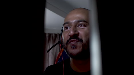 hombre indio calvo con auriculares golpeando la cabeza de un lado a otro escuchando música y siendo interrumpido por una llamada