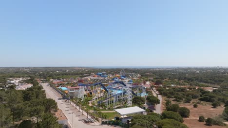 bright-blue-orange-water-slides-park-in-algarve-portugal,-Aerial-reverse-dolly