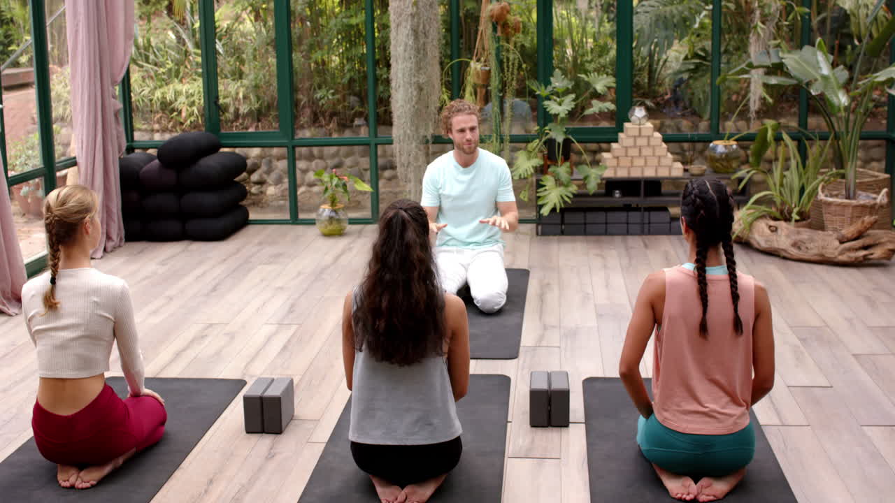 Gruppo di persone sedute su tappetini in uno studio con pareti in vetro, durante la pratica yoga