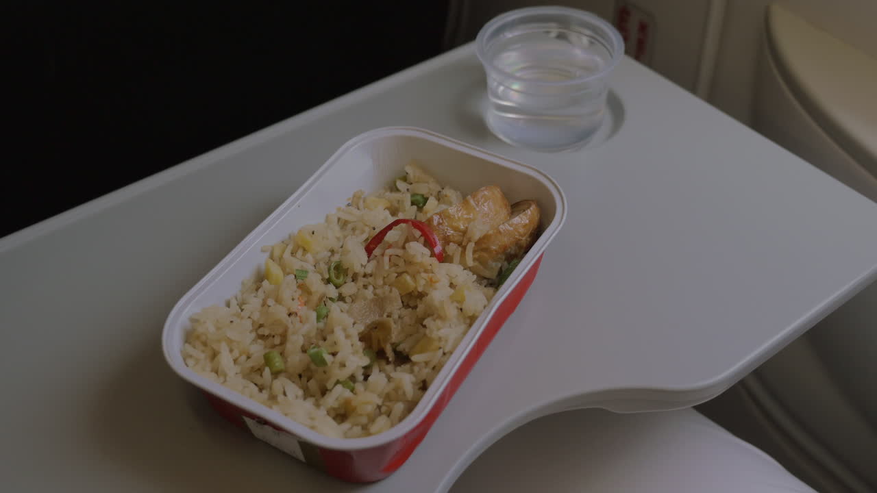 en el avión en la mesa hay vajilla desechable con un plato de arroz y pollo y una mujer come comida con un tenedor