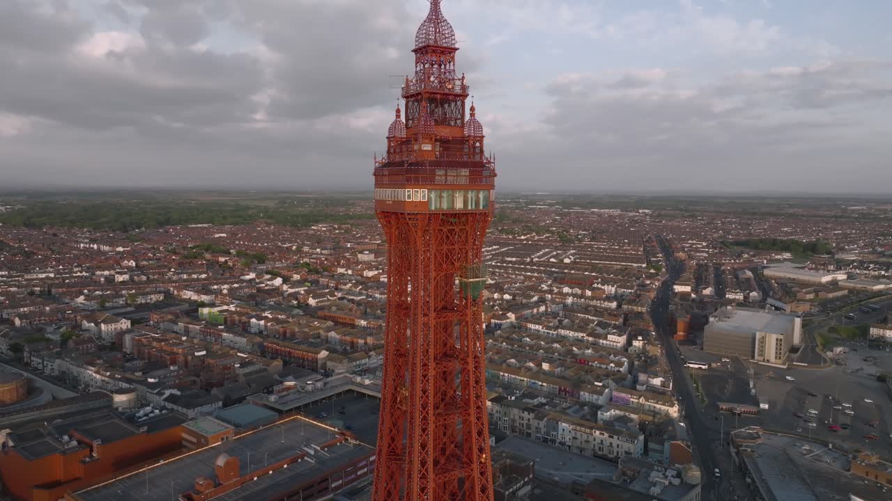 Blackpool Tower red painted steel glowing at golden hour with urban sprawl behind. Lancashire, UK.