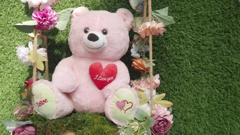 pink teddy bear sitting on a swing with flowers