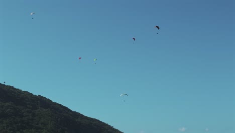 siete parapentes se elevan en armonía cerca de una montaña verde en un hermoso día soleado