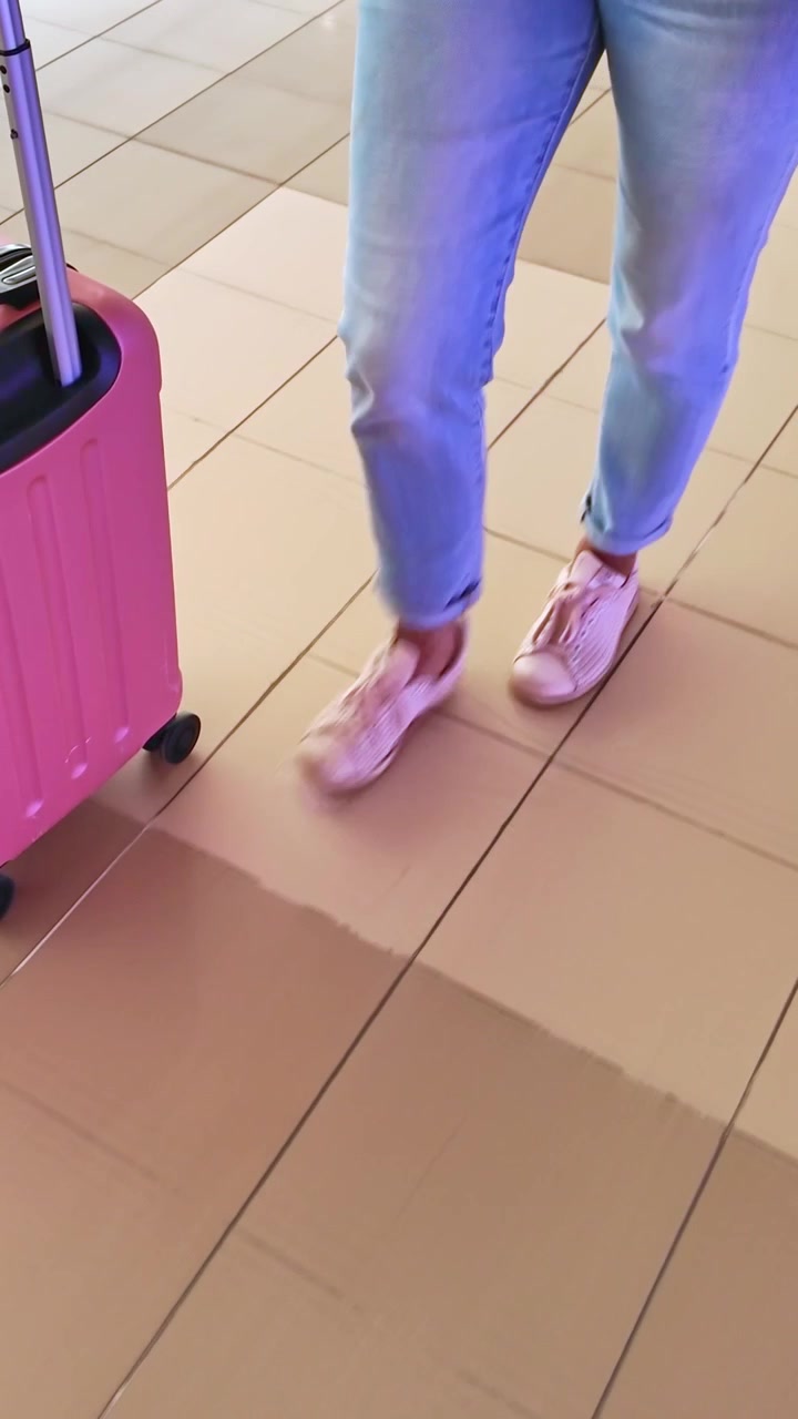 Mujer caminando con una maleta rosa en la terminal del aeropuerto.