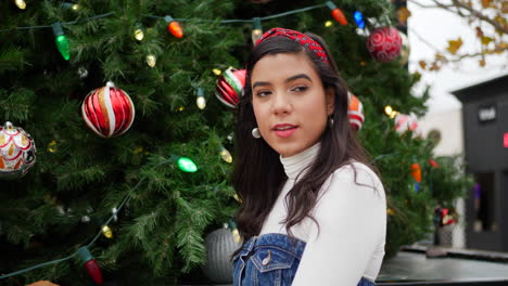 una hermosa mujer hispana al aire libre en la ciudad haciendo sus compras de regalos navideños con un árbol de navidad