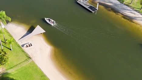 a boat glides along a tranquil canal beside a sandy beach and lush greenery.