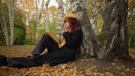 woman sits under tree in solitude, reading book thoughtfully in autumn forest, surrounded by golden leaves, she embraces calm, inspiration, and creativity