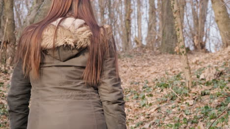 back view of a long haired woman in winter jacket walking deep in forest during winter on a sunny day