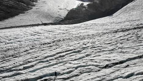 aerial flyover over a hiker walking across the ice of the allalin glacier near saas-fee in valais, switzerland on a sunny day in the swiss alps with a pan up view from the crevasses up to the peaks