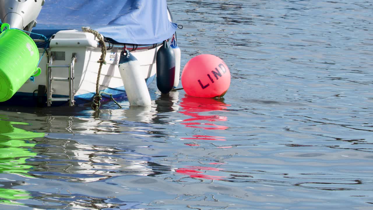 Motorboat stern with green and red buoys gently moving on sunlit harbor water, daytime