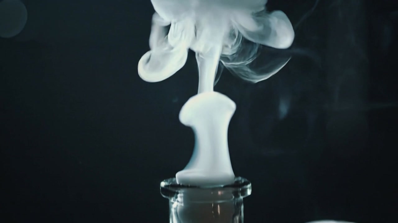 Hand placing tool above flask, producing white vapor expanding on dark wooden tabletop, cork beside