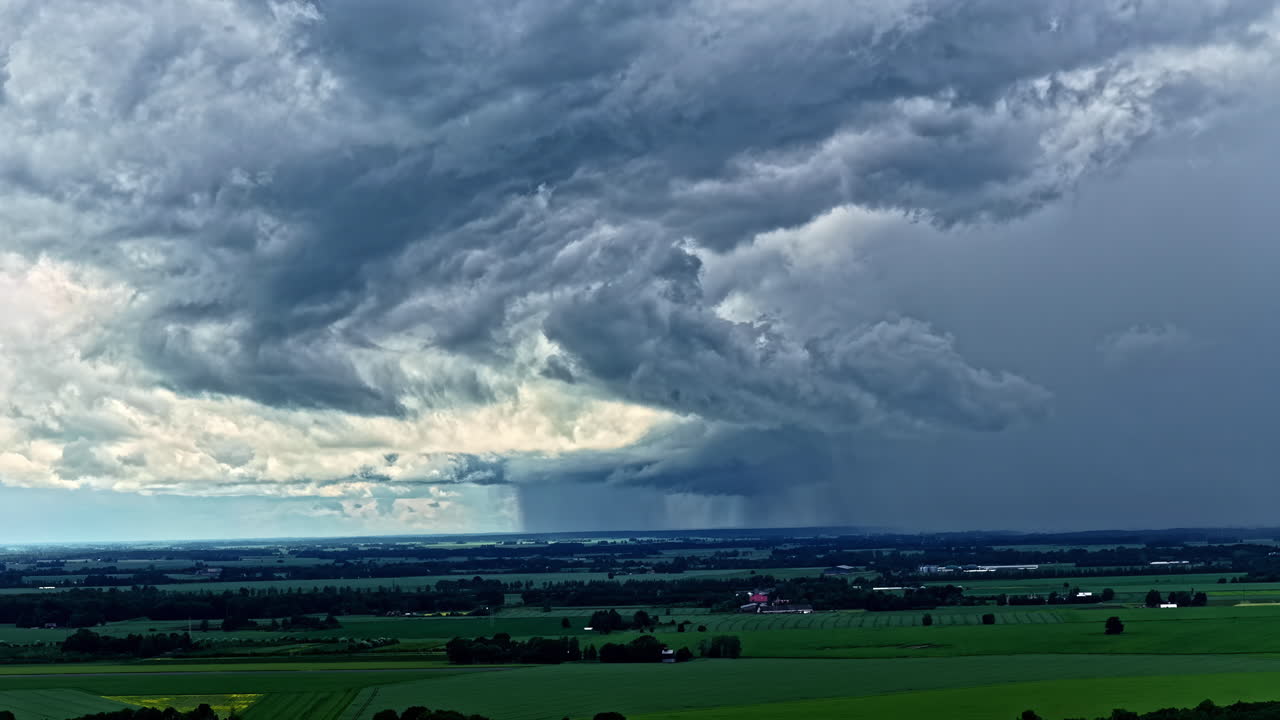 Dramatic rainstorm seen approaching over rural farmland under swirling clouds