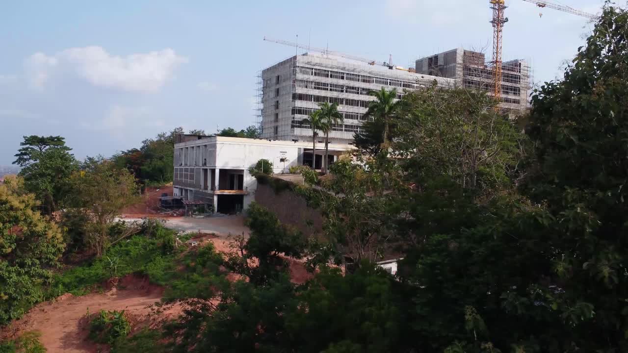 Lush greenery in the foreground as camera pans left to reveal reconstruction of Premier Hotel on Mokola Hill.