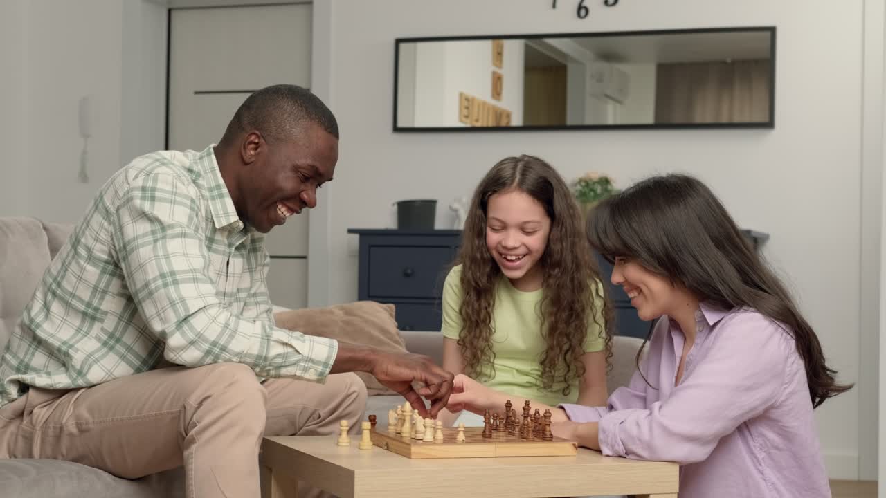 Happy family of three people of different races play chess at home in the living room