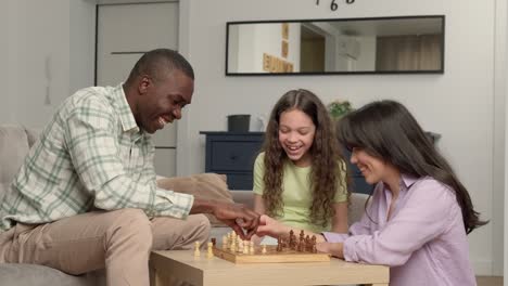 Happy family of three people of different races play chess at home in the living room