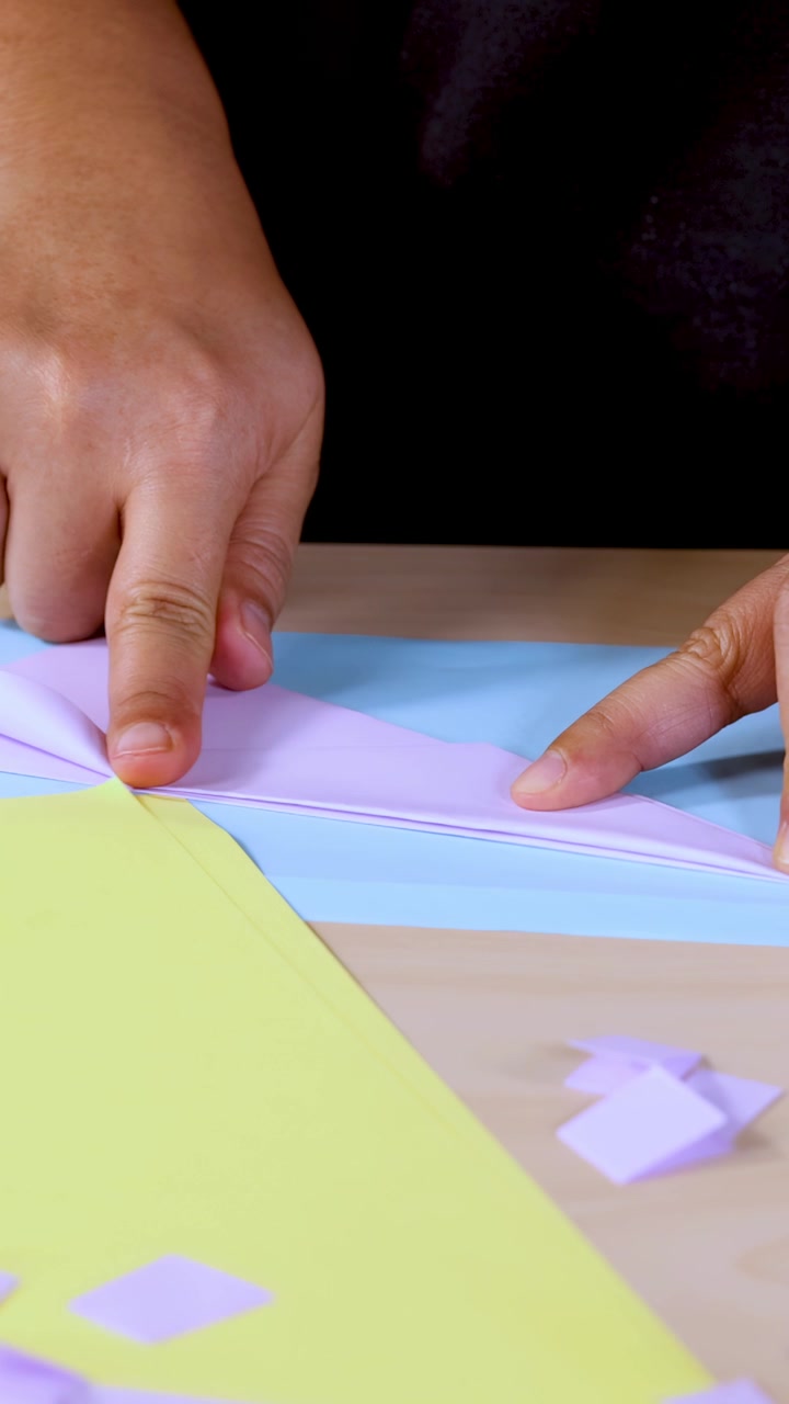 Person’s hands folding pastel paper for origami craft, close-up, steady camera, bright lighting