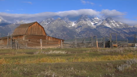un antiguo granero surge de una pradera con los grand tetons al fondo