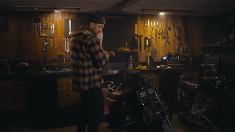 A-happy-mechanic-in-a-checkered-shirt-puts-his-little-daughter-on-a-motorcycle-and-talks-about-his-workshop