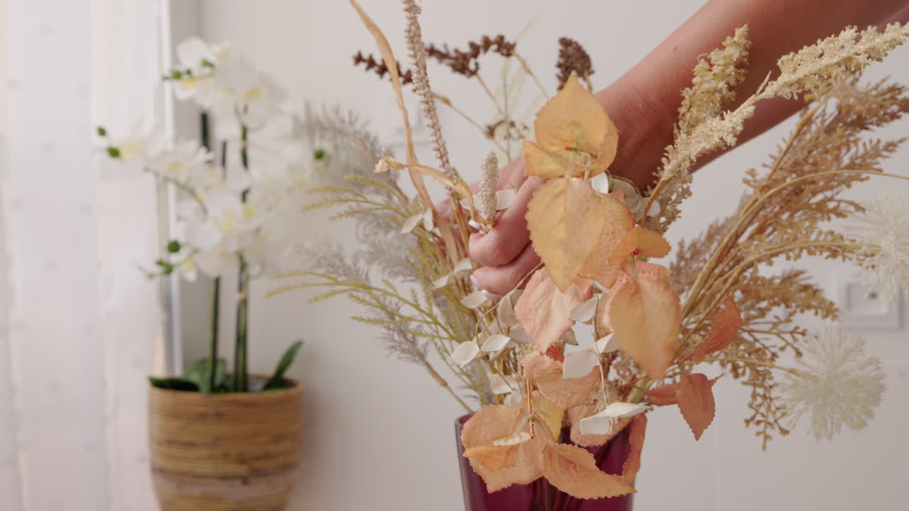 Donna che sistema un bouquet di fiori e piante secchi in un vaso decorativo a casa.