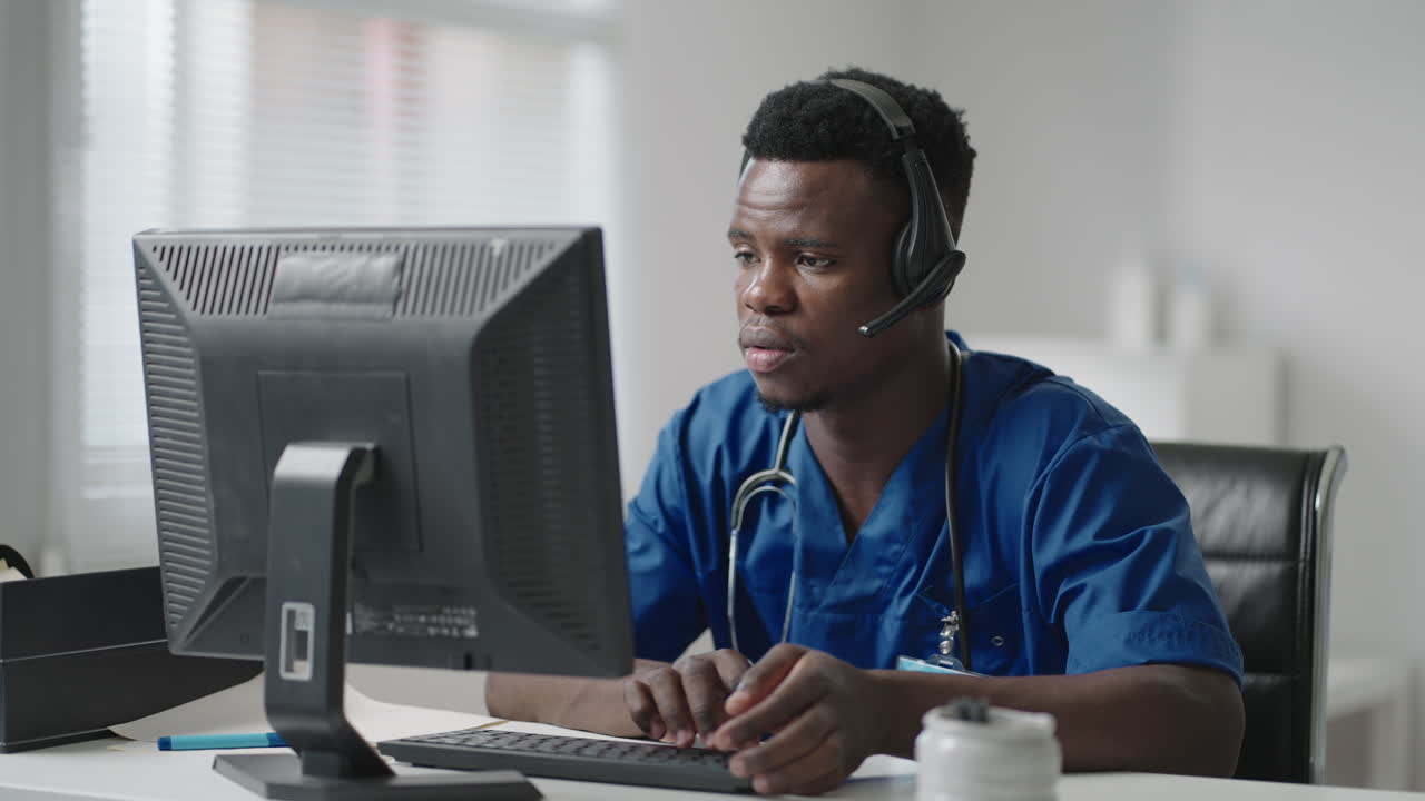 Medico o infermiere afroamericano con cuffie e computer che lavora in ospedale. Giovane medico o terapista professionista che consulta un paziente utilizzando la comunicazione a distanza e parlando in webcam
