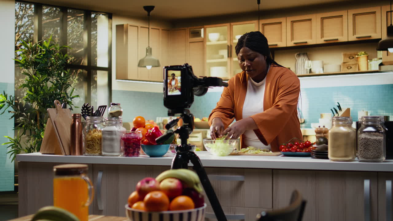 Vlogger di cucina, afroamericana, che taglia foglie d'insalata per la preparazione dei pasti