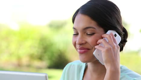 Businesswoman-having-coffee-while-working-on-laptop-and-talking-on-phone