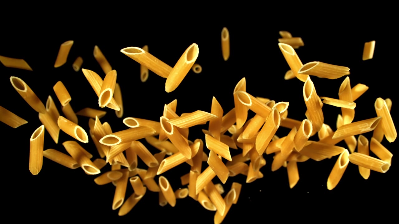 Pasta penne che cade e galleggia al rallentatore su sfondo nero