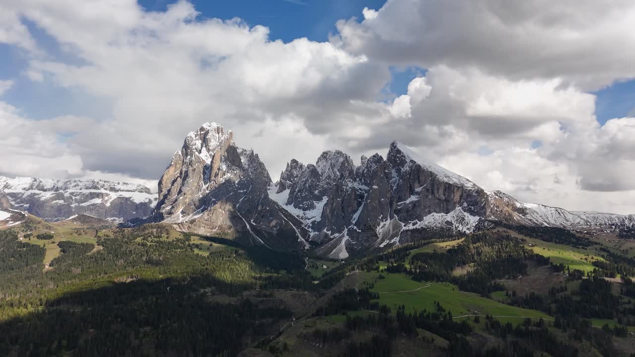 Drone footage captures Alpe di Siusi’s green valleys and Sassolungo peaks under a partly cloudy sky in the Dolomites, South Tyrol, Italy