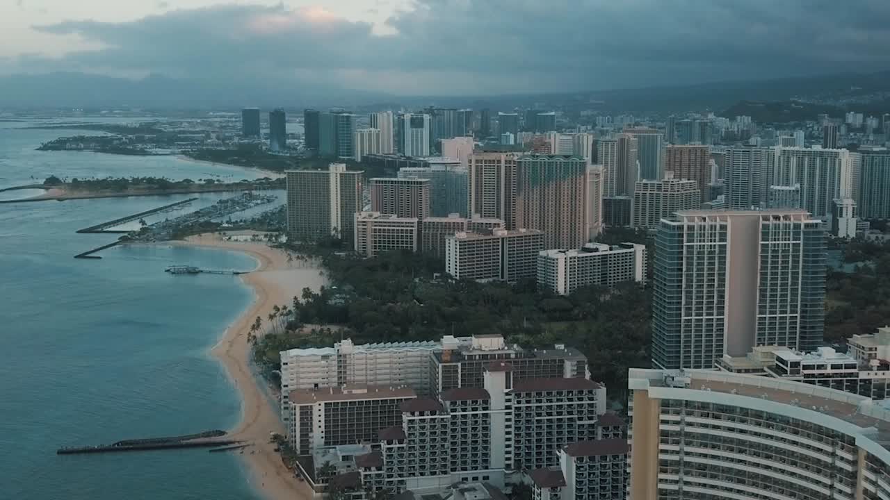 Drone aereo in lenta panoramica che sorvola lo skyline colorato di Honolulu al tramonto a Oahu, Hawaii, con la spiaggia di Waikiki come punto di interesse speciale
