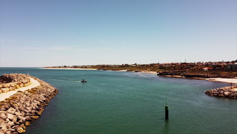 Aerial-view-of-wild-coastline-entrance-of-harbor-with-boat-sailing