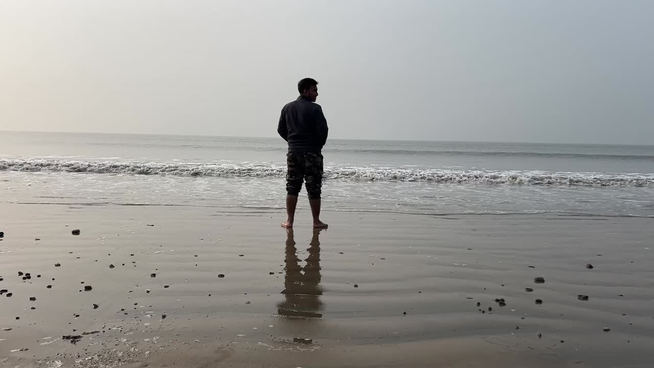 fotografía trasera de un hombre de pie en la costa de una playa con pequeñas olas durante el verano en bengal, india