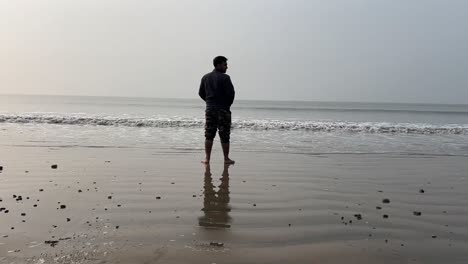 rear shot of a man standing on coastline of a beach with small waves during summer in bengal, india