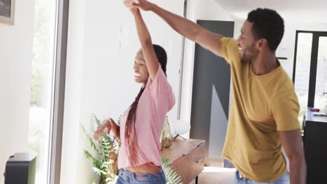 happy african american couple holding hands and dancing in living room, in slow motion