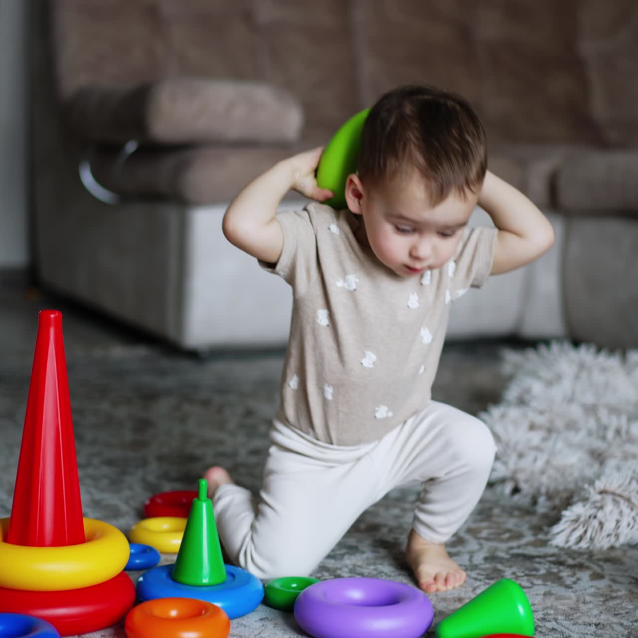 One year old toddler playing with his toys on the floor. Kid takes a ring from pyramid and walks away with it