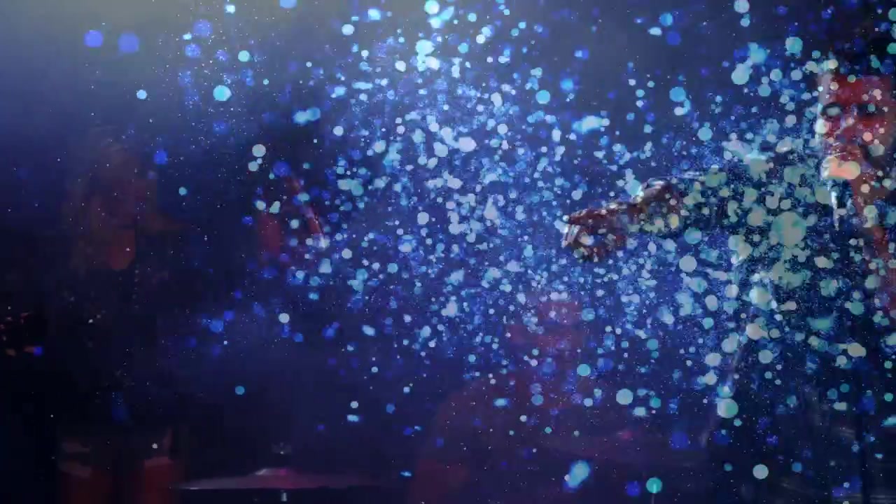 Two singers singing left, cue sparking blue confetti, male singer stepping into cloud leading music