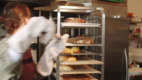 woman taking bread from oven with shovel while working in bakery